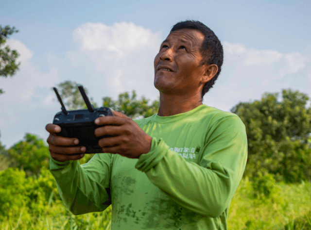 an Indigenous man wearing a green shirt operates a drone